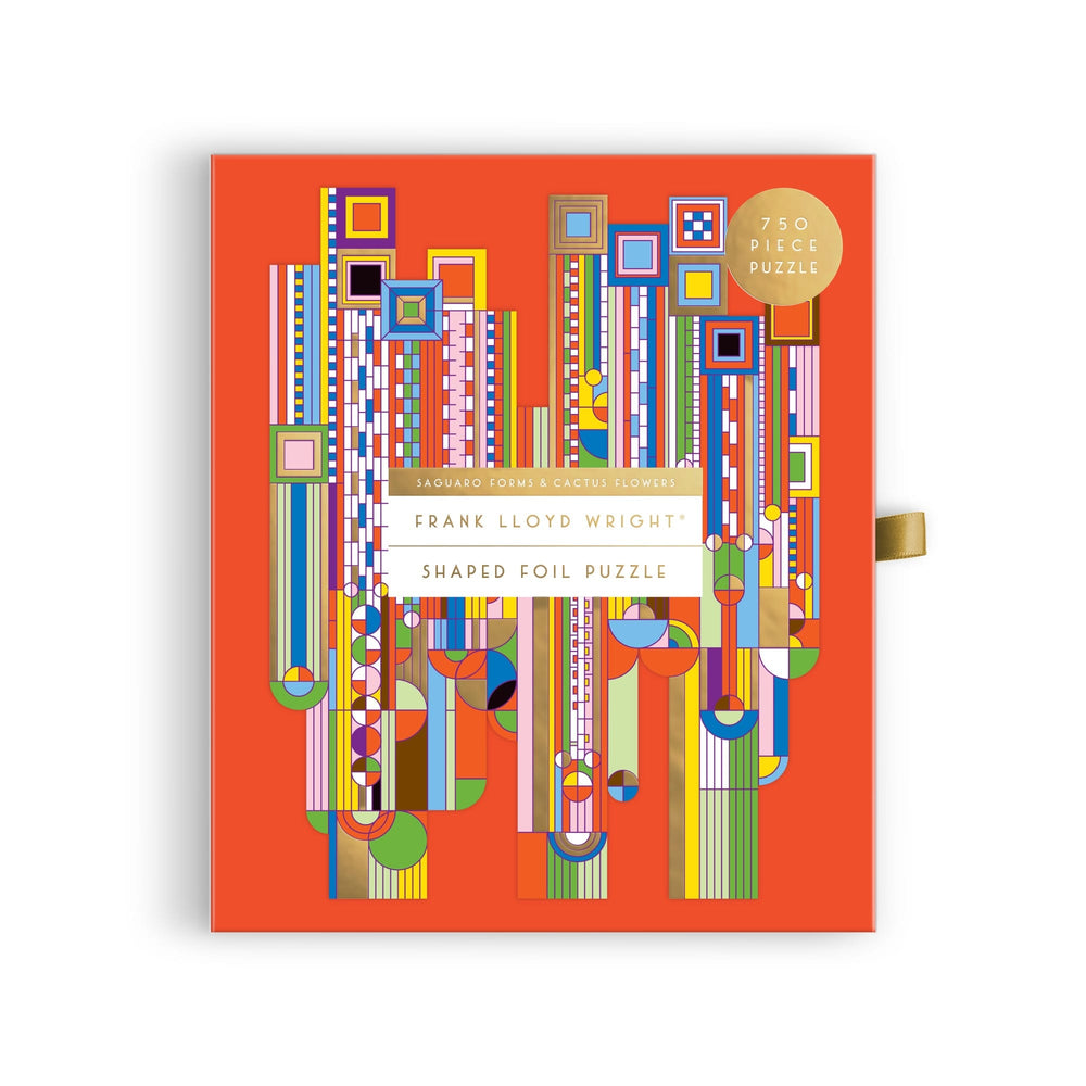 A bright orange puzzle box features a colorful geometric design inspired by Frank Lloyd Wright, with bold shapes and foil accents. The label reads “Frank Lloyd Wright Foundation Saguaro Cactus & Forms 750 Piece Shaped Foil Puzzle.”.