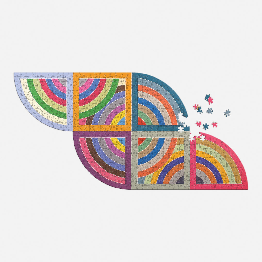 The Frank Stella Harran II 750 Piece Shaped Puzzle by Frank Stella features colorful, abstract rainbow curves with a few loose pieces on the right side, displayed on a white background and packed in a drawer box.