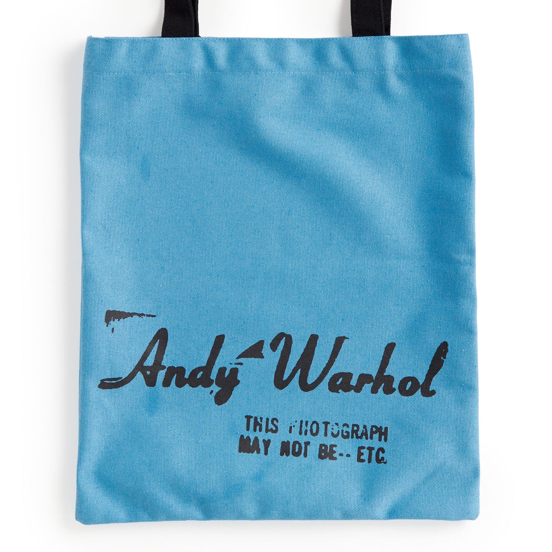 The Warhol Soup Can Volume 3 Canvas Tote Bag by the Andy Warhol Foundation features a light blue color, black handles, "Andy Warhol" in handwritten-style font, and "THIS PHOTOGRAPH MAY NOT BE..." printed below in black.