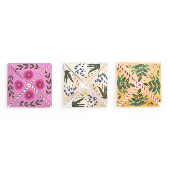 Three colorful origami fortune tellers, each with hand-painted pink, blue, and yellow floral designs, are arranged in a row—beautiful stationery inspired by Joy Laforme Charm Cards from Joy Laforme.
