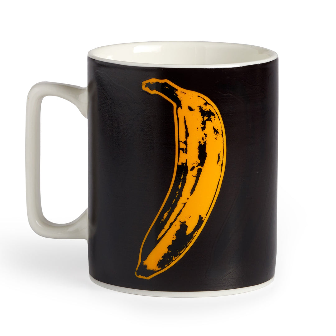 The Andy Warhol Banana Color Changing Ceramic Mug by Andy Warhol features a bold yellow banana graphic inspired by Warhol, with a black exterior, white interior and handle.