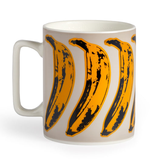 The Andy Warhol Banana Color Changing Ceramic Mug by Andy Warhol features a white ceramic design with a vibrant yellow and black banana pattern inspired by pop art, revealing colors as the mug heats up.