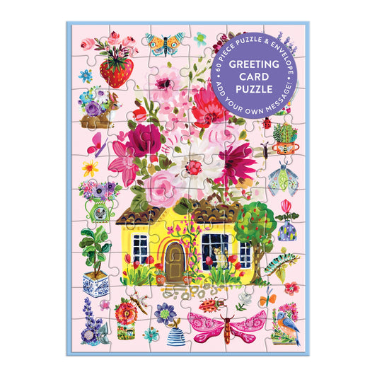 The Buzzy Bouquets Greeting Card Puzzle by Jennifer O Lewis / August Wren features a yellow cottage with a floral roof, vibrant flowers, butterflies, and garden accents on a light background. A purple label in the top right highlights card details.