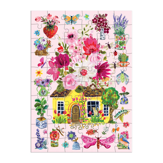 The Buzzy Bouquets Greeting Card Puzzle by Jennifer O Lewis/August Wren features a yellow cottage with a brown roof among vibrant flowers, dragonflies, and butterflies on a pink background, outlined by whimsical puzzle pieces.