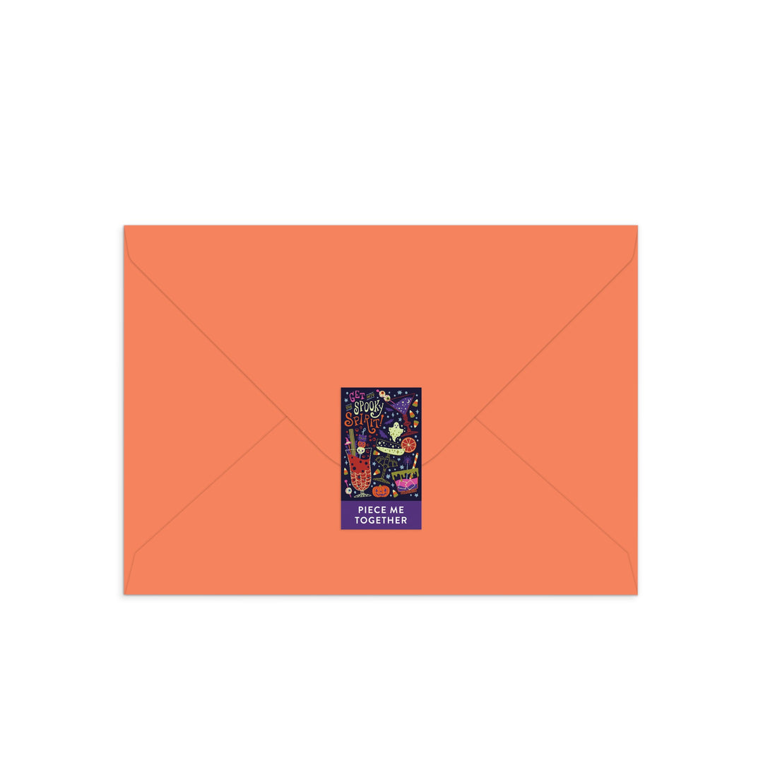 A vibrant orange envelope sealed with a sticker featuring two cats on a puzzle and the phrase Piece Me Together—the Get into the Spooky Spirit Greeting Card Puzzle by Camille Chew is the purrfect interactive card for any occasion.