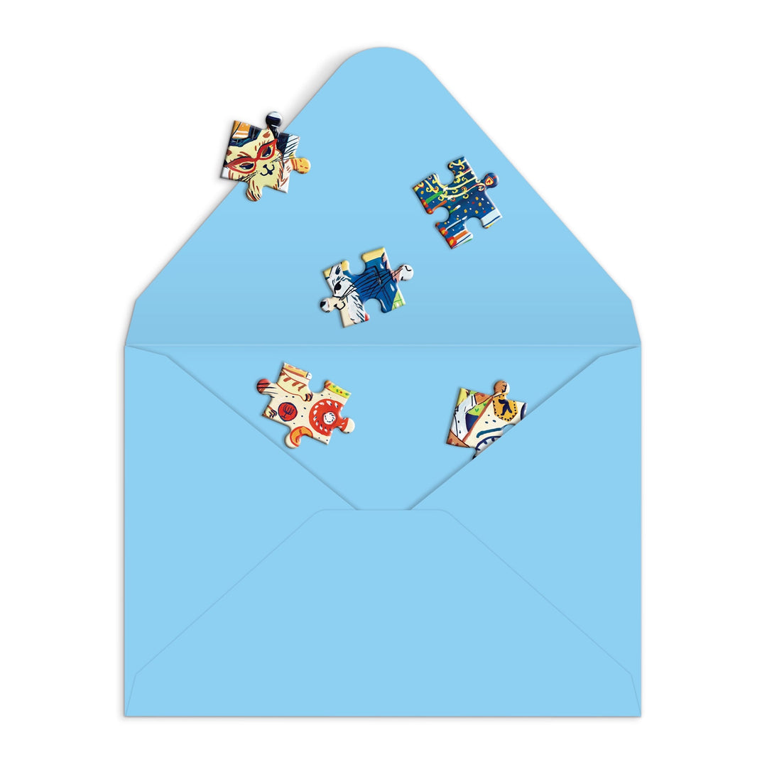 The Happy Hanukcats Greeting Card Puzzle by Anna Ivanir features six festive cat jigsaw pieces in a light blue open envelope—offering a joyful, interactive Hanukkah greeting for cat lovers and puzzle fans alike.