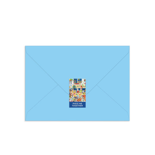 A closed light blue envelope with a festive feline sticker and the text PIECE ME TOGETHER holds the Happy Hanukcats Greeting Card Puzzle by Anna Ivanir—an interactive Hanukkah card with a playful cat-themed puzzle inside.