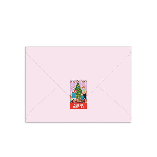A light pink envelope sealed with a festive sticker features the Joanna Clay Meowy Christmas Greeting Card Puzzle, showcasing a charming feline-themed illustration and the words PIECE ME TOGETHER on a red background.