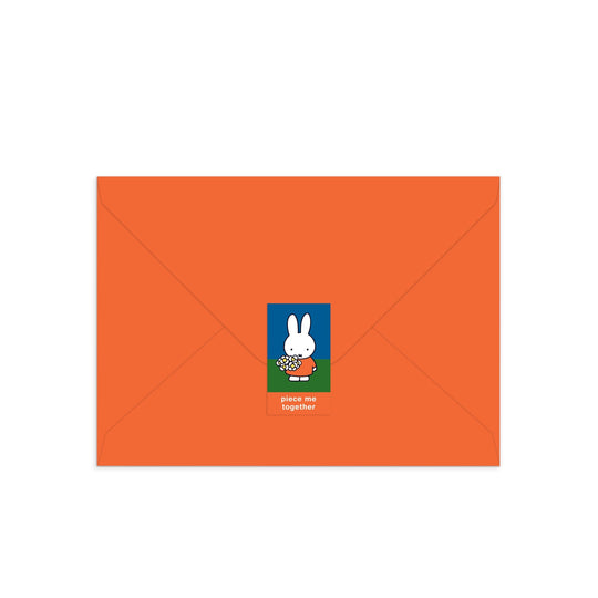 An orange envelope with a Miffy Birthday Greeting Card Puzzle sticker featuring white cartoon bunny Miffy holding flowers and the words "piece me together.