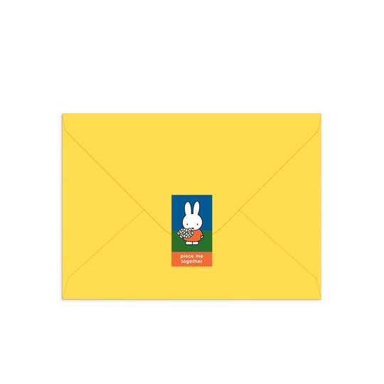 A closed yellow envelope displays a center sticker with Miffy, the white cartoon rabbit, holding flowers and “piece me together” on a red background. Product: Miffy with Flowers Greeting Card Puzzle by Miffy.