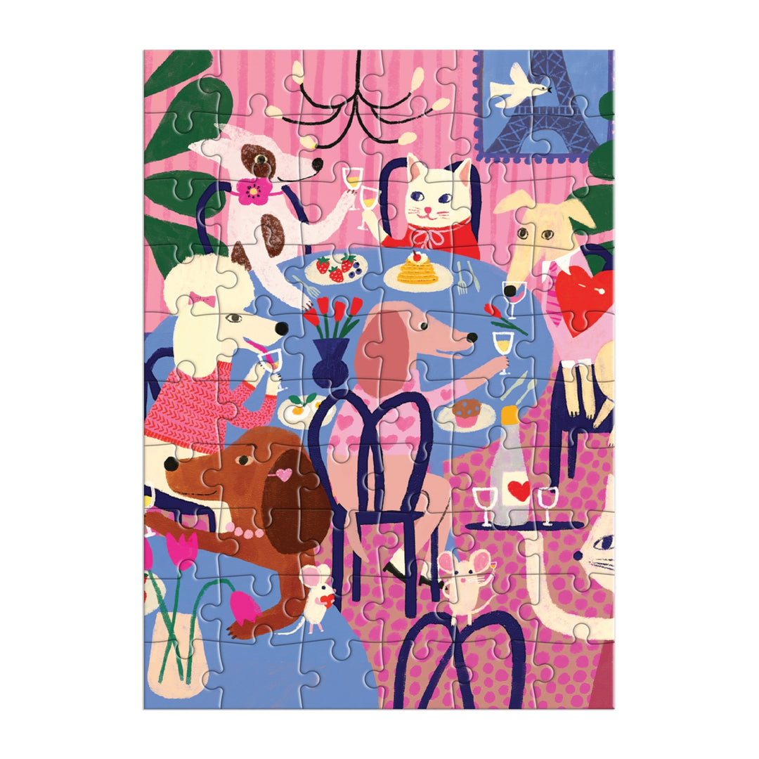 The Paws for Love Greeting Card Puzzle by Anne Bentley features a colorful indoor scene with dogs and a cat around a table, surrounded by flowers, plants, and a chandelier in vibrant pink, blue, and purple tones.