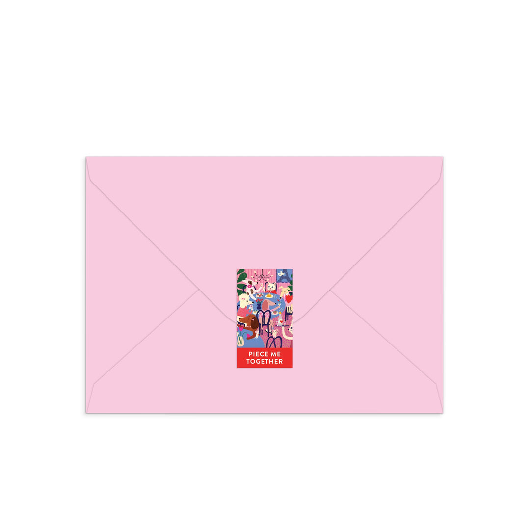 A light pink envelope sealed with a colorful rectangular sticker inspired by Anne Bentley’s Paws for Love Greeting Card Puzzle, featuring cartoon animals, people, and “PIECE ME TOGETHER” in bold white letters at the bottom.