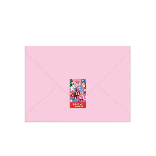 A light pink envelope sealed with a colorful rectangular sticker inspired by Anne Bentley’s Paws for Love Greeting Card Puzzle, featuring cartoon animals, people, and “PIECE ME TOGETHER” in bold white letters at the bottom.