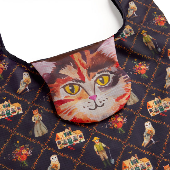 The Cottage Cats Packable Nylon Tote by Anja Riebensahm is a reusable bag with a flap featuring a realistic cat face and dark diamond-patterned fabric adorned with whimsical cats in clothes, owls, bouquets, and tiny houses.