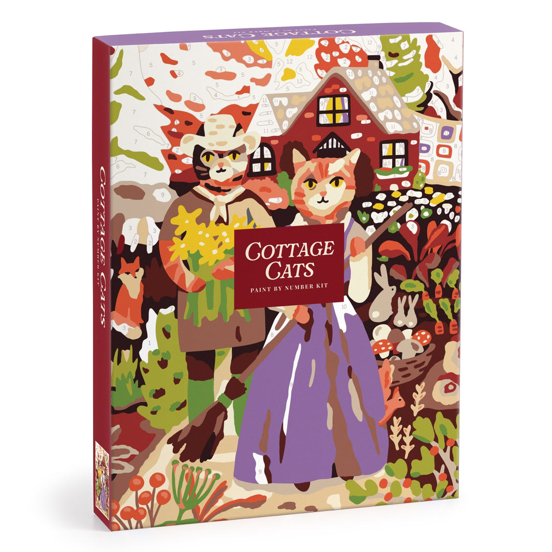 The Cottage Cats 9 x 12 Paint by Number Kit by Anja Riebensahm features two cats in traditional clothes standing before a cozy cottage, surrounded by colorful plants and flowers on the box illustration.