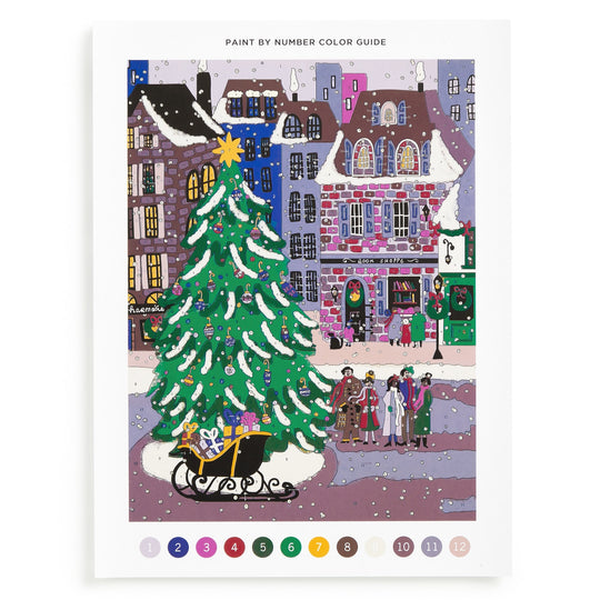 The Joy Laforme Christmas Square 9 x 12 Paint by Number Kit features a snowy town square with a decorated tree, sleigh of gifts, festive buildings, and people. Numbered color circles are displayed below the vibrant holiday scene.