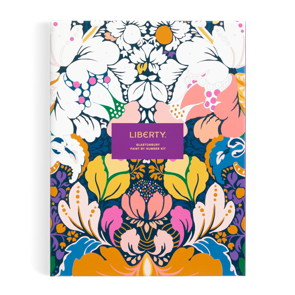 A vibrant, symmetrical floral pattern in blues, pinks, oranges, purples, and white centers on a purple LIBERTY label. Inspired by Glastonbury, this is the Liberty London 9 x 12 Paint by Number Kit with premium acrylic paints.
