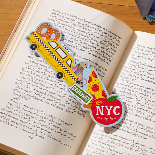 The Big Apple Paper Bookmark by Holly Maguire features NYC icons like a taxi, pretzel, pigeon, pizza slice, and apple with landmarks and text such as BROADWAY and The Big Apple—perfect for marking your place in style.