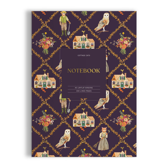 The Anja Riebensahm Cottage Cats A5 Premium Notebook features a dark purple cover with cottages, floral bouquets, owls, and vintage-dressed cats. The center label reads: Cottage Cats NOTEBOOK.