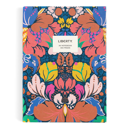 The Liberty London Glastonbury Premium A5 Notebook features a vibrant, symmetrical floral cover in orange, yellow, pink, and blue with a white label stating “LIBERTY GLASTONBURY. A5 NOTEBOOK 300 PAGES” and high-quality paper inside.