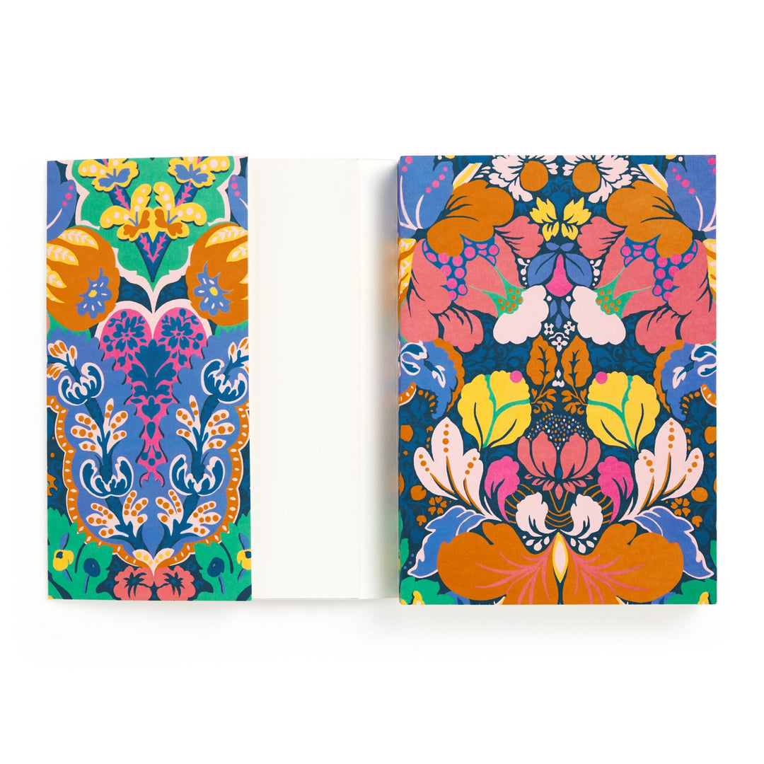 The Liberty Glastonbury Premium A5 Notebook by Liberty London features vibrant orange, blue, green, and pink floral and botanical covers. The inside is blank and white, contrasting elegantly with its colorful decorative exterior.