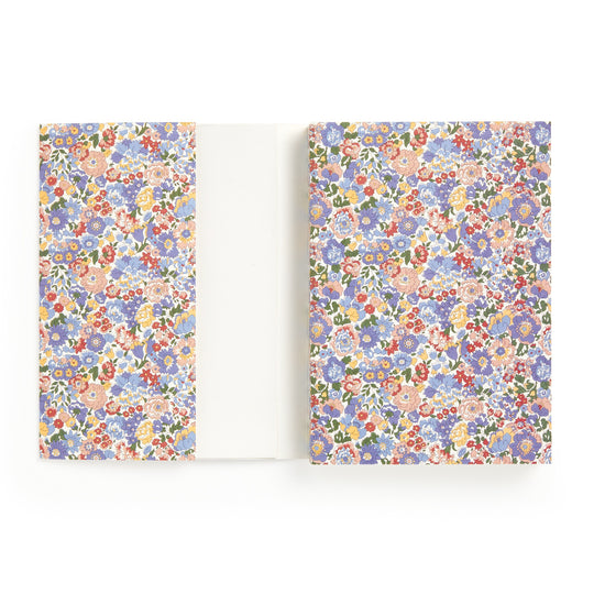 The Liberty London Nell, Annie and May Premium A5 Notebook is open, revealing a colorful floral-patterned cover and endpapers with small pink, blue, red, and orange flowers. Inside are blank white pages.