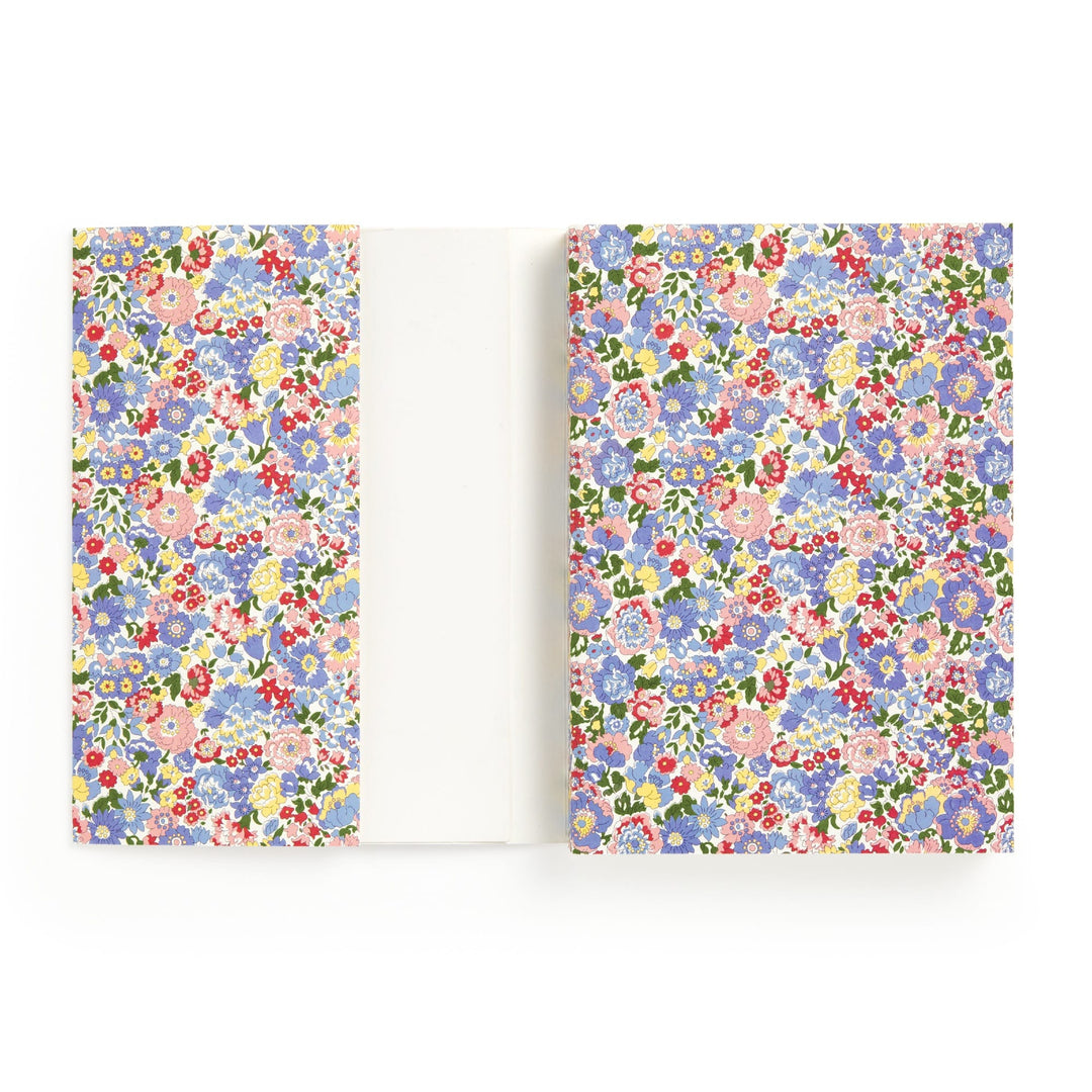 The Liberty London Liberty Nell, Annie and May Premium A5 Notebook features a white cover with colorful blue, pink, red, and purple floral patterns, inside flaps to match, and blank pages for writing or drawing.
