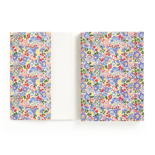 The Liberty London Liberty Nell, Annie and May Premium A5 Notebook features a white cover with colorful blue, pink, red, and purple floral patterns, inside flaps to match, and blank pages for writing or drawing.