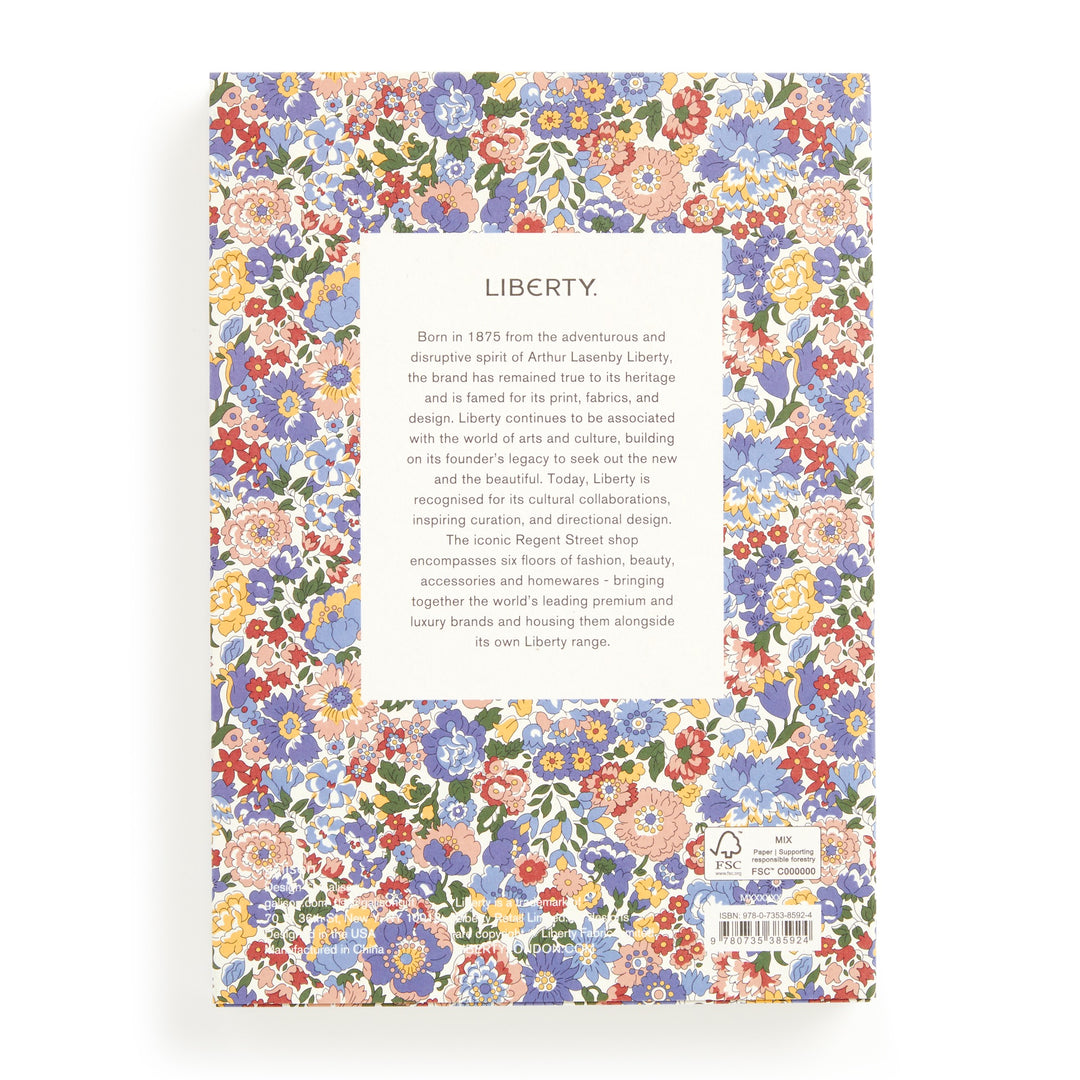 The Liberty Nell, Annie and May Premium A5 Notebook by Liberty London features a vibrant red, blue, yellow, and white floral back cover with a central white box detailing the brand’s history and design philosophy.