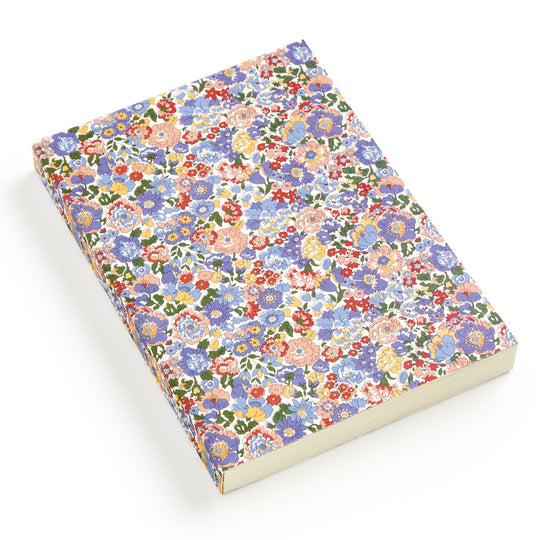 The Liberty Nell, Annie and May Premium A5 Notebook by Liberty London features a vibrant red, blue, pink, and yellow floral design on white, inspired by Liberty London’s signature patterns. The closed A5 notebook rests on a white surface.