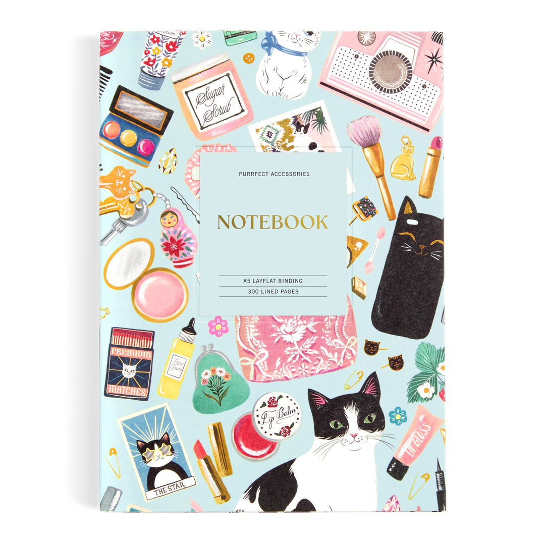 The Christine De Carvalho Purrfect Accessories Premium A5 Notebook features feline, makeup, book, and perfume illustrations on a light blue cover. Includes 300 lined pages and a Notebook center label—perfect for sophisticated stationery lovers.