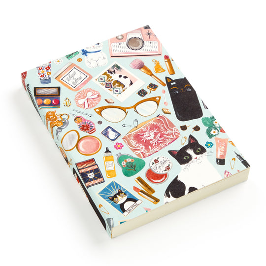 The Purrfect Accessories Premium A5 Notebook by Christine De Carvalho features a vibrant cover with chic feline illustrations, glasses, cosmetics, makeup items, perfume, brushes, and flowers on a light blue background.