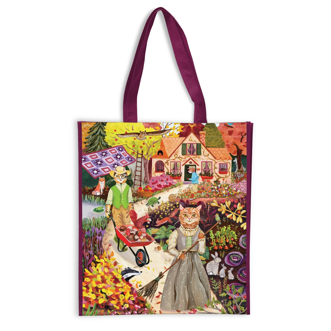 The Cottage Cats Reusable Shopping Bag by Anja Riebensahm showcases two autumn-dressed cats gardening near a cozy house, with fall leaves, flowers, apples in a wheelbarrow, and a patchwork quilt in the scene.