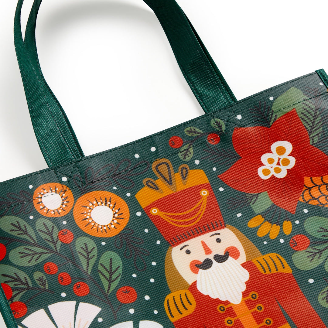 The Merry Nutcracker Reusable Shopping Bag by Sandra Hutter features festive holiday artwork with a nutcracker, red flowers, pinecones, and green foliage on a dark green background with scattered white dots and green handles.