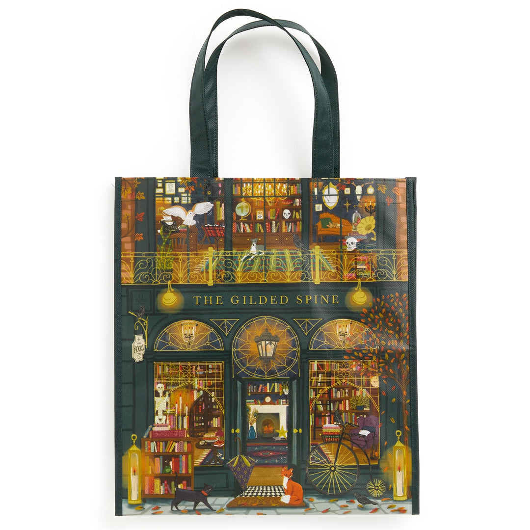 The Gilded Spine Reusable Shopping Bag by Sally Wilson features a cozy, two-story bookstore with books, animals, autumn leaves, and warm yellow lights. A person and cat read outside, adding to its charming illustrated design.