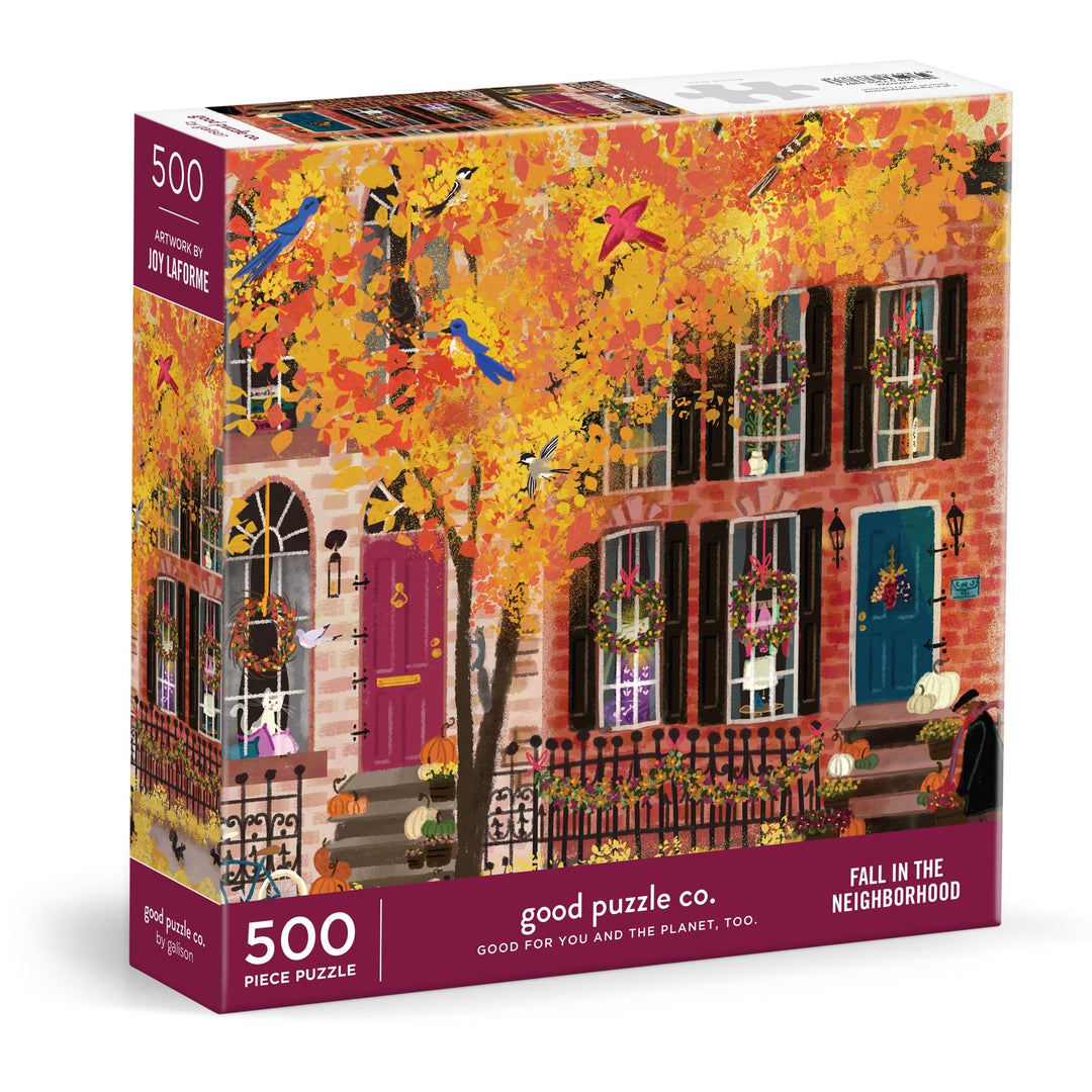 The Good Puzzle Co. Fall in the Neighborhood 500pc Puzzle by Joy Laforme shows a vivid autumn city street with colorful row houses and fall foliage, made from recycled materials.