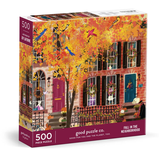 The Good Puzzle Co. Fall in the Neighborhood 500pc Puzzle by Joy Laforme shows a vivid autumn city street with colorful row houses and fall foliage, made from recycled materials.