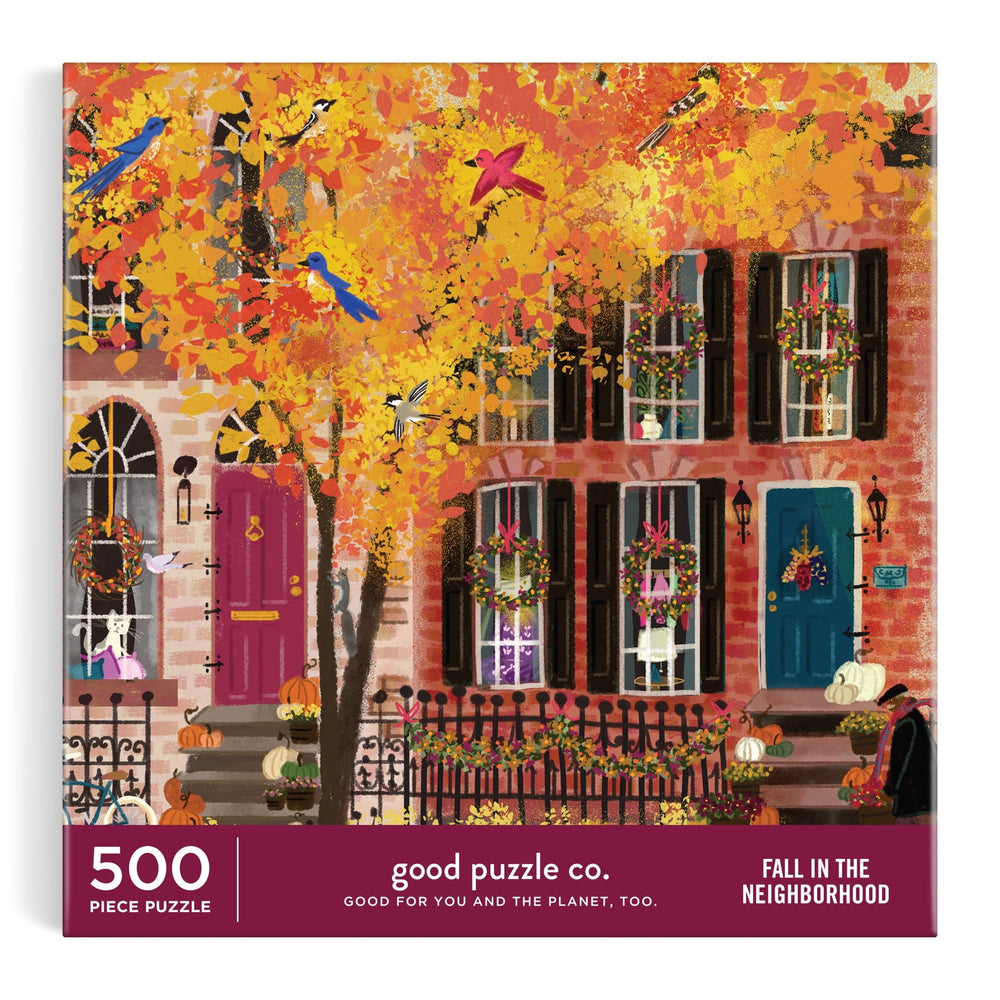 The Good Puzzle Co. Fall in the Neighborhood 500pc Puzzle by Joy Laforme features an autumn city street with brownstones, colorful doors, leaves, pumpkins, and perched birds; crafted from recycled materials.
