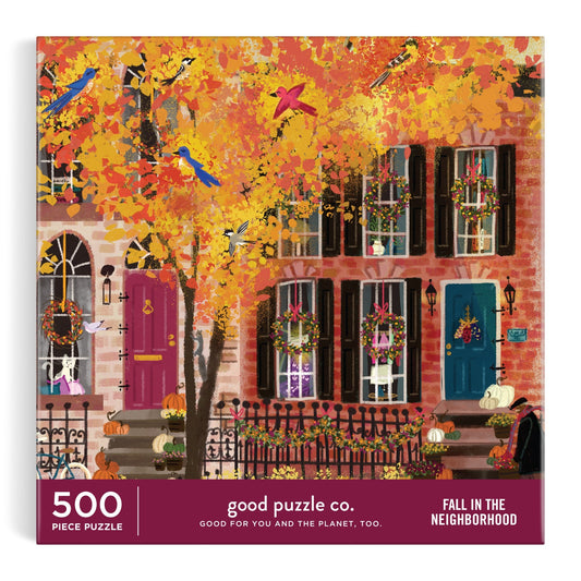The Good Puzzle Co. Fall in the Neighborhood 500pc Puzzle by Joy Laforme features an autumn city street with brownstones, colorful doors, leaves, pumpkins, and perched birds; crafted from recycled materials.