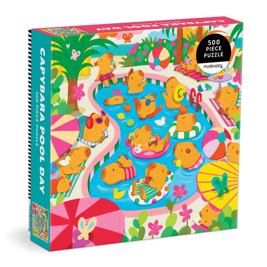The Valerie Nelson Capybara Pool Day 500 Piece Family Puzzle features cartoon capybaras relaxing in a vibrant pool scene with floaties, umbrellas, and tropical plants—perfect fun for the whole family.