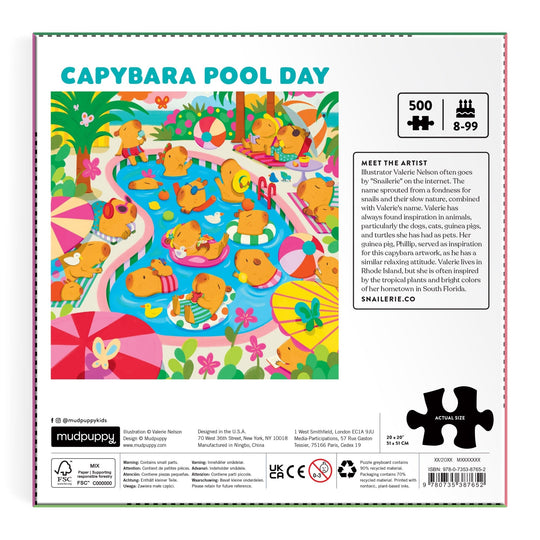 A vibrant illustration of capybaras relaxing poolside appears on the back of the Valerie Nelson Capybara Pool Day 500 Piece Family Puzzle. Lush greenery, umbrellas, and pool floats complete this fun family puzzle scene.